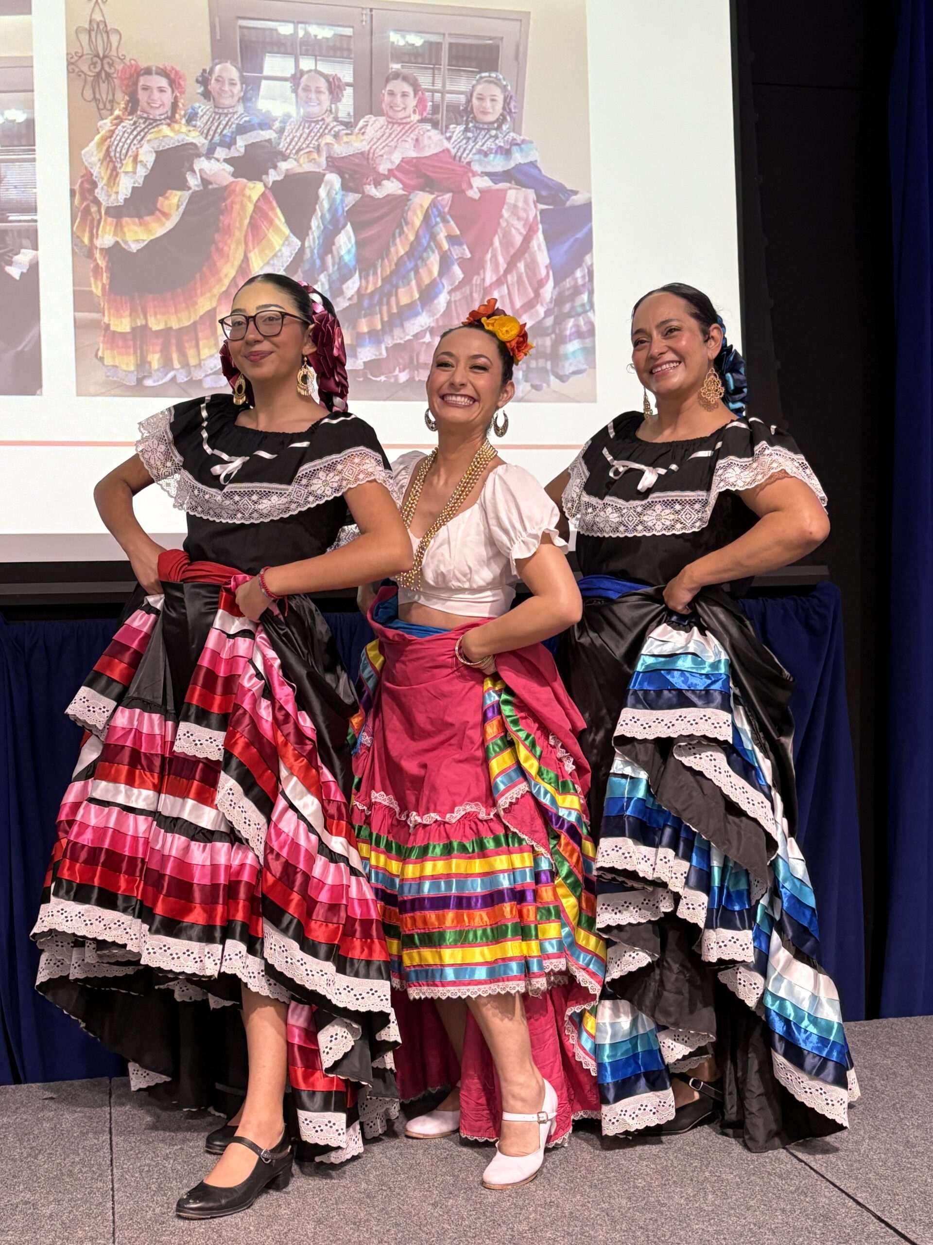 Three dancers in traditional Mexican dresses on a stage
