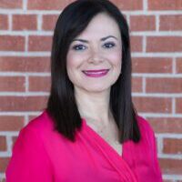 Smiling woman in pink blouse, brick background.