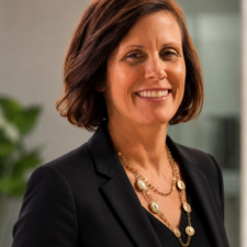 Woman with brown hair wearing gold chain necklace and black shirt.